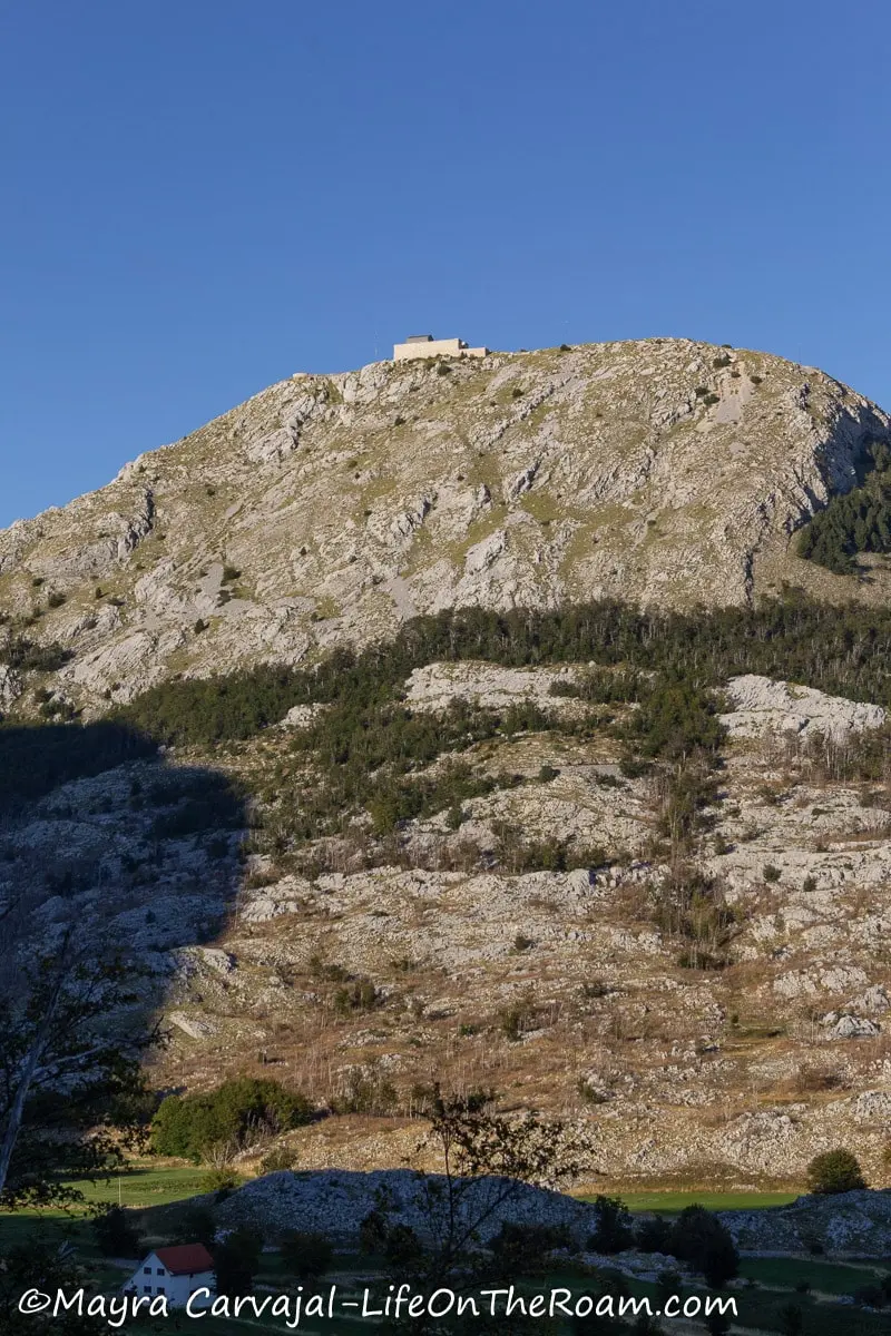 Distant view of a rectangular building sitting at the top of a mountain partially covered by vegetation