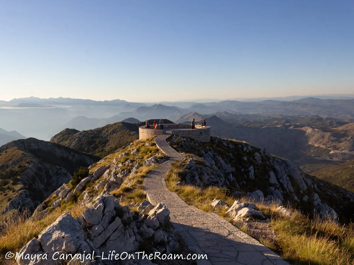 A round viewing platform on top of a mountain with a path along the ridge