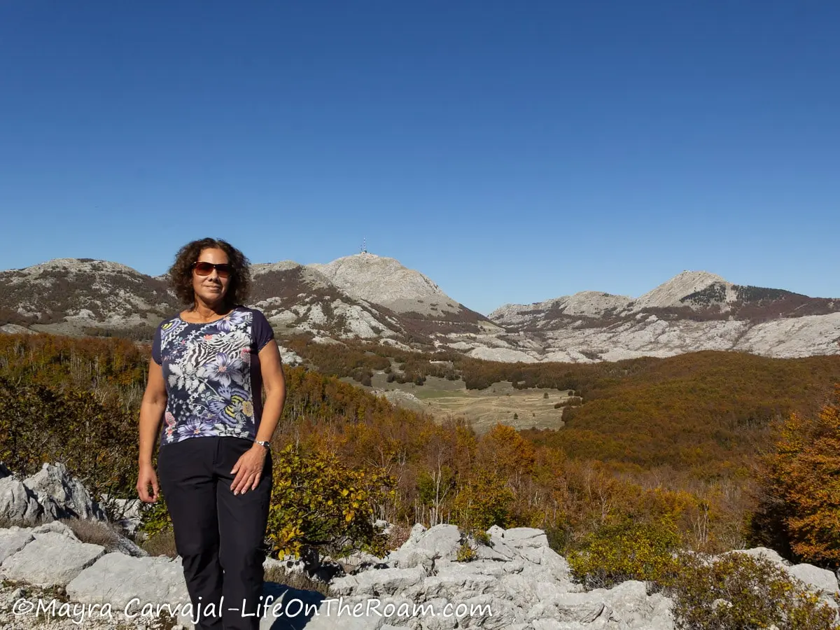 Mayra standing on a trail with views of mountain peaks partially covered by vegetation