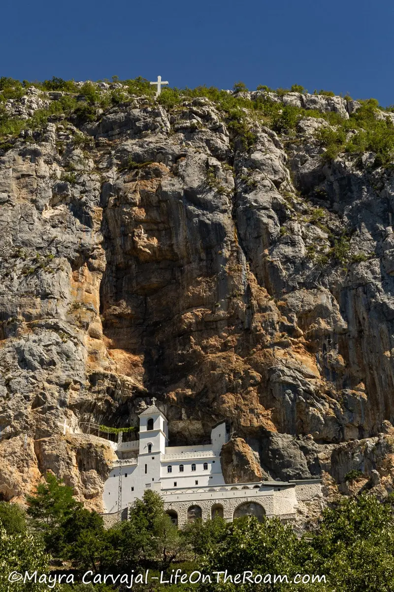 A monastery built inside a cliff with a cross at the top of the rock