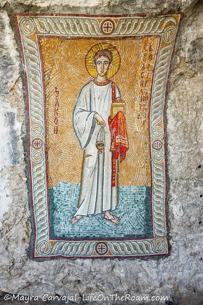 A mosaic in the surface of a cave depicting a saint with white robe on a blue floor