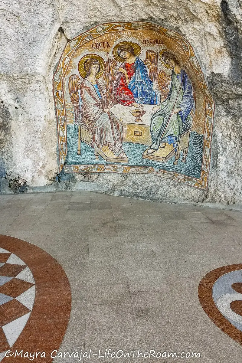 A mosaic on a cave-like room depicting three angels around a table