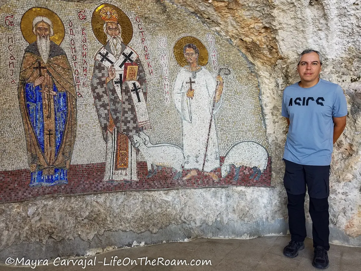 A man standing next to a mosaic showing three saints with three saints