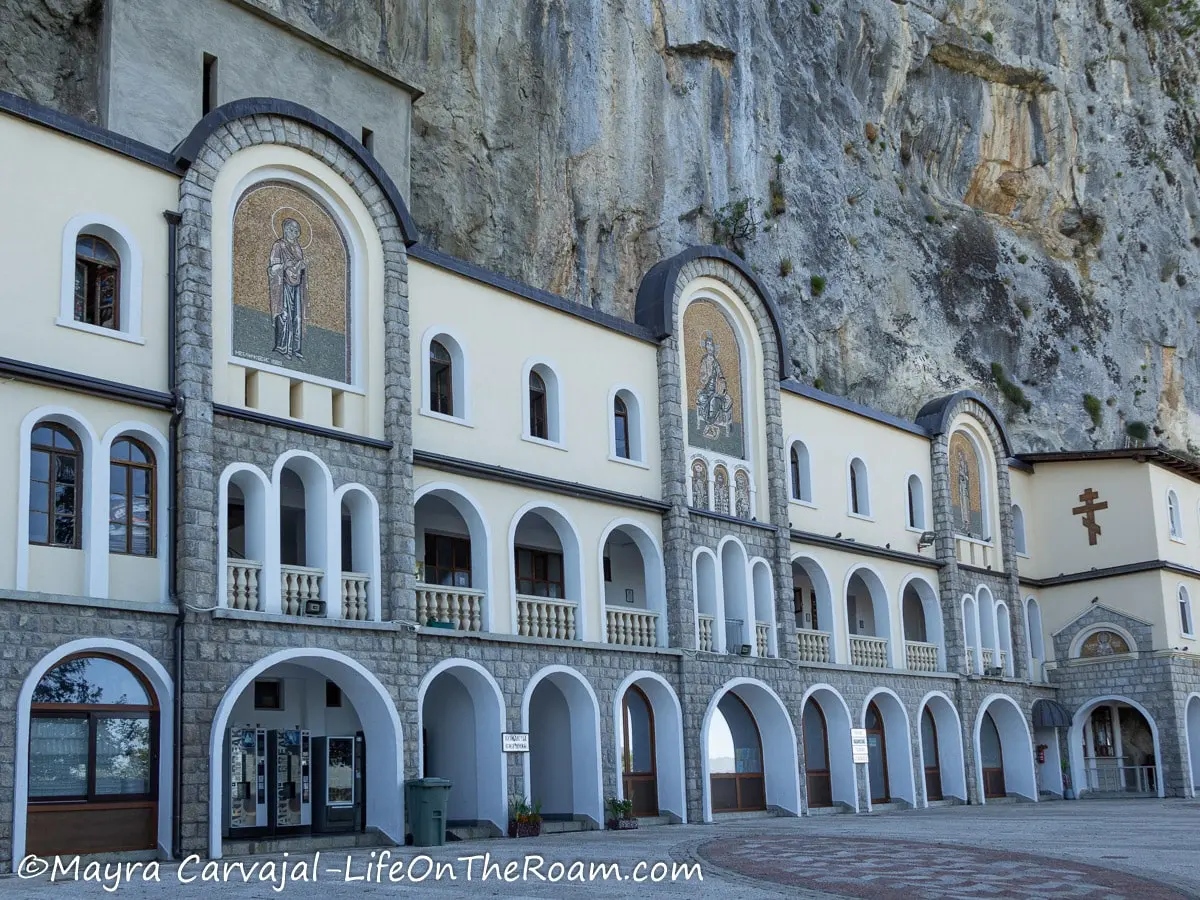 A building against a cliff with arched windows and doors and mosaics on the upper section