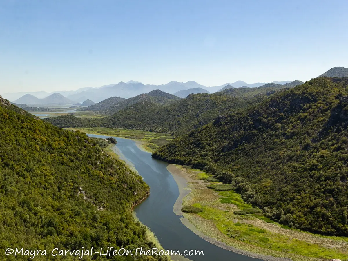 View of a river along a green valley with mountains in the distance