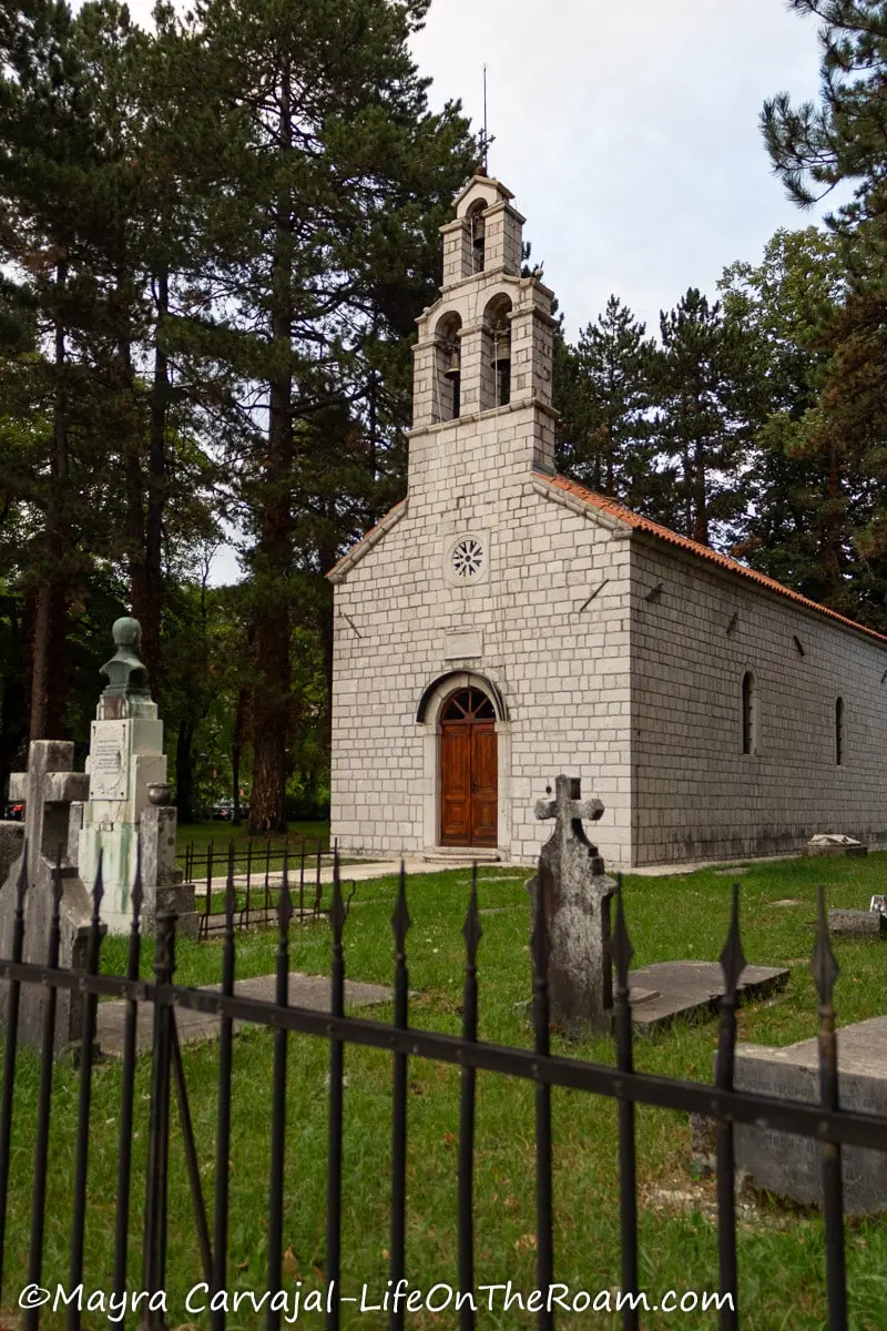 An old stone church with a three-bell tower surrounded by a black metal fence