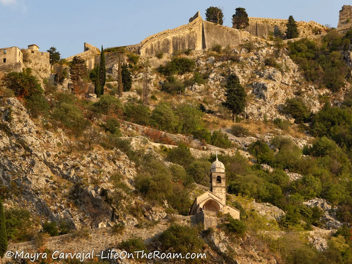 A small old church up in a hill with the ruins of a fortress in the mountaintop