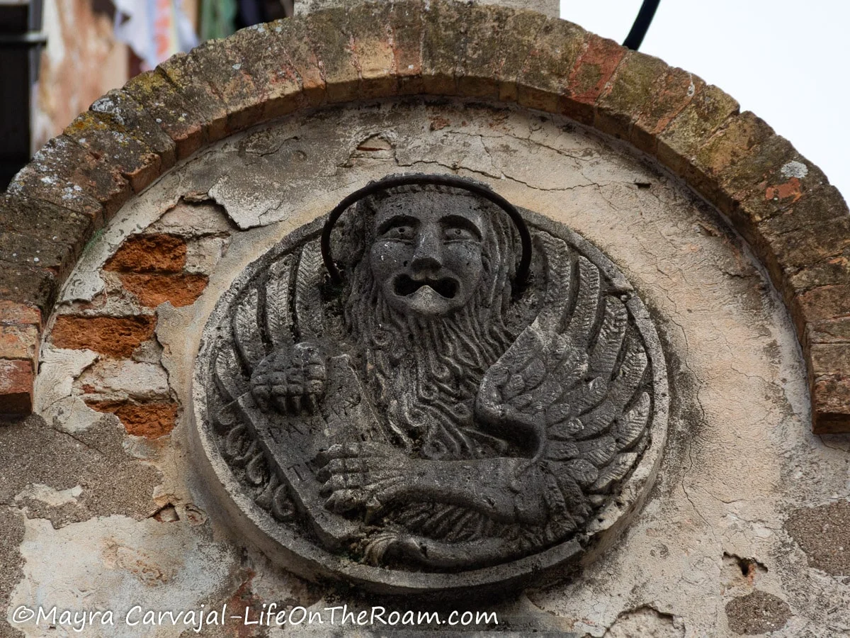 A stone relief depicting a winged lion holding a Bible, inside an arch
