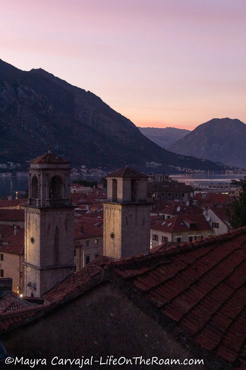 View of two bell towers at sunset with mountains and water in the distance