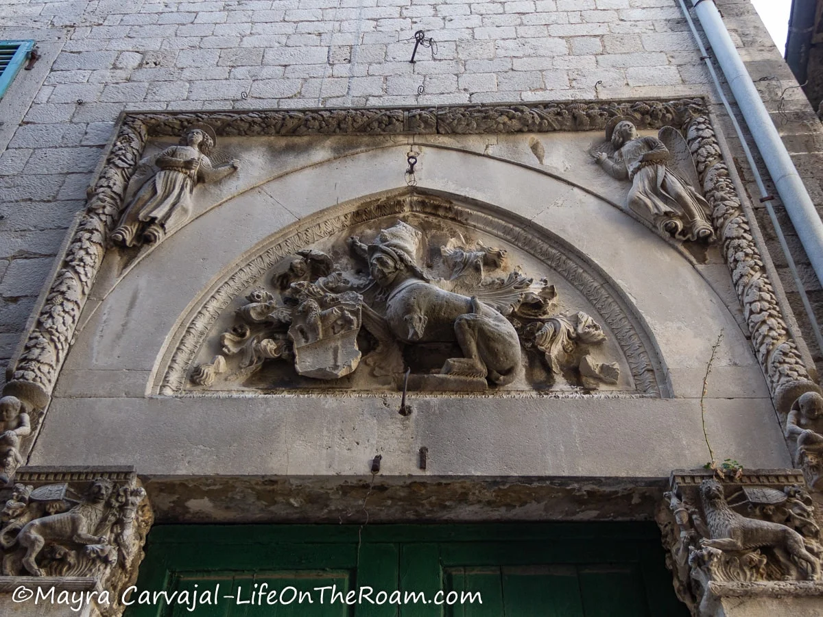 A tympanum decorated with bas-relief in stone depicting a lion, swirly decorations, and angels