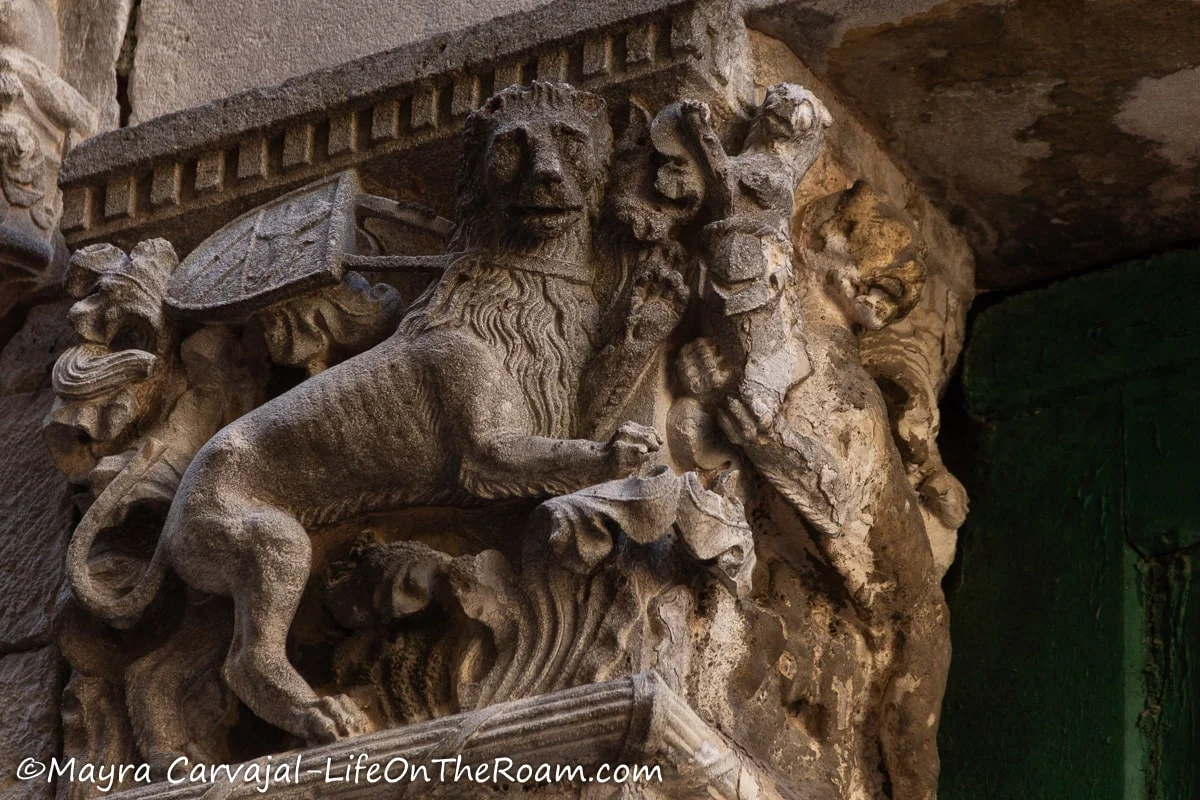 A bas-relief on the upper section of a door trim depicting a lion with a coat of arms with swirly decorations around