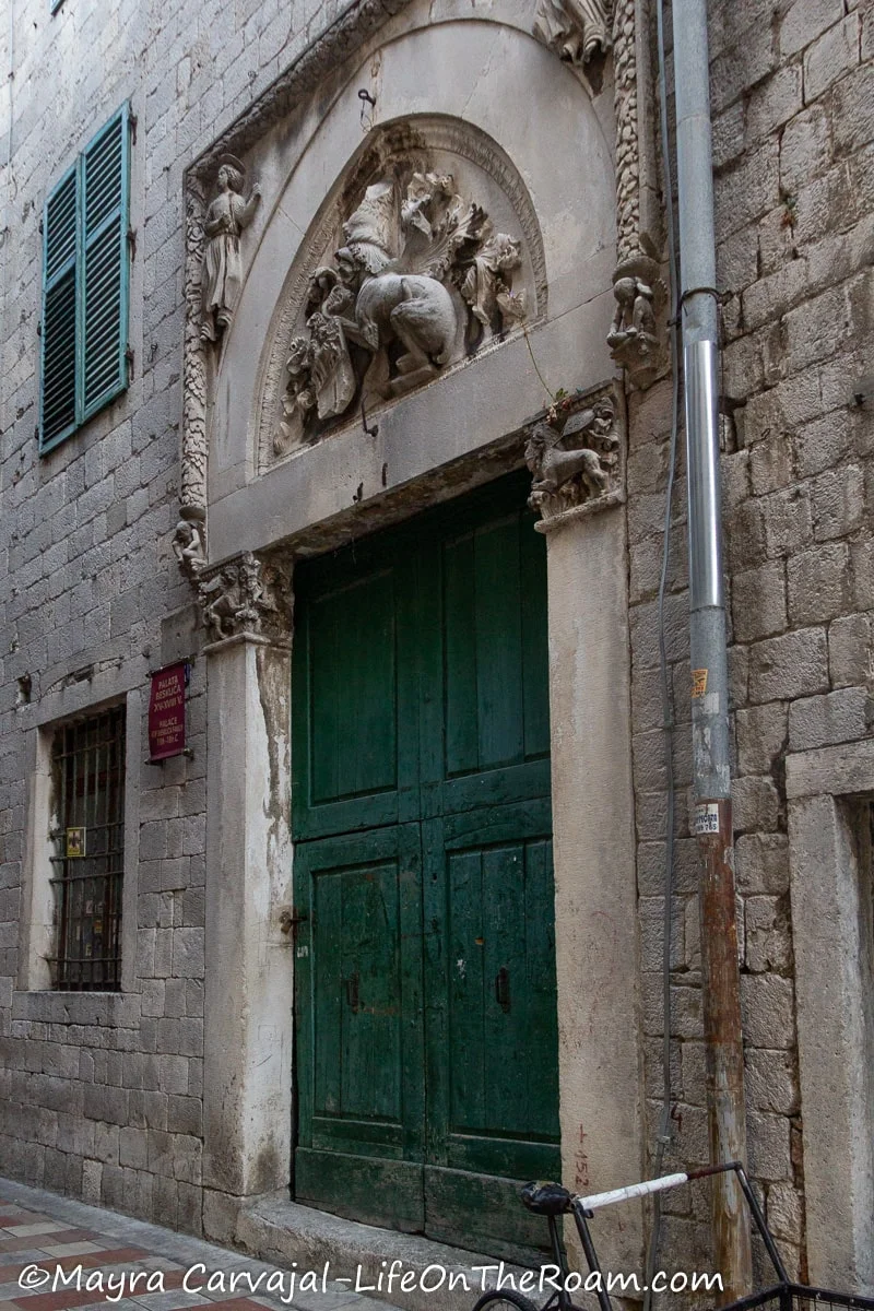 A tall green double door surrounded in a stone building with a decorated tympanum above