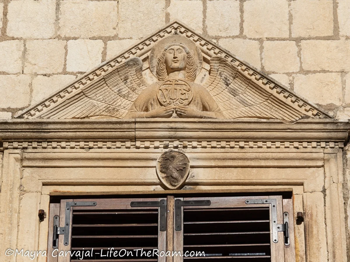 A pediment at the top of a window with an angel and a dragon as a small coat of arms
