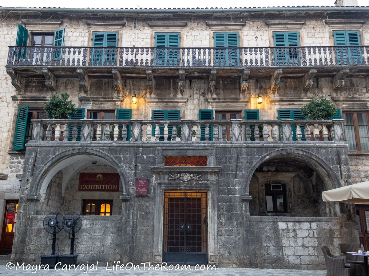 A 3-storey building with arched windows on the ground floor and balconies on the upper floors and blue shutters