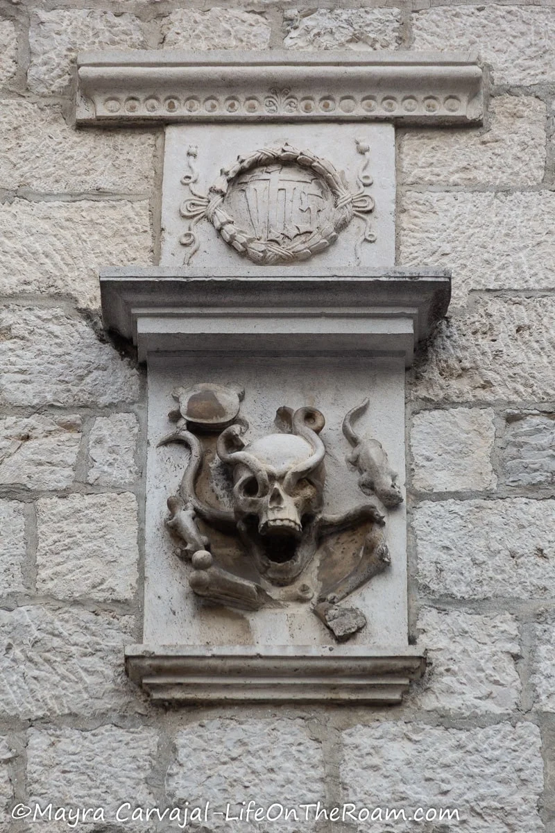 Stone figures on a stone wall depicting a skull, serpents, and a rodent