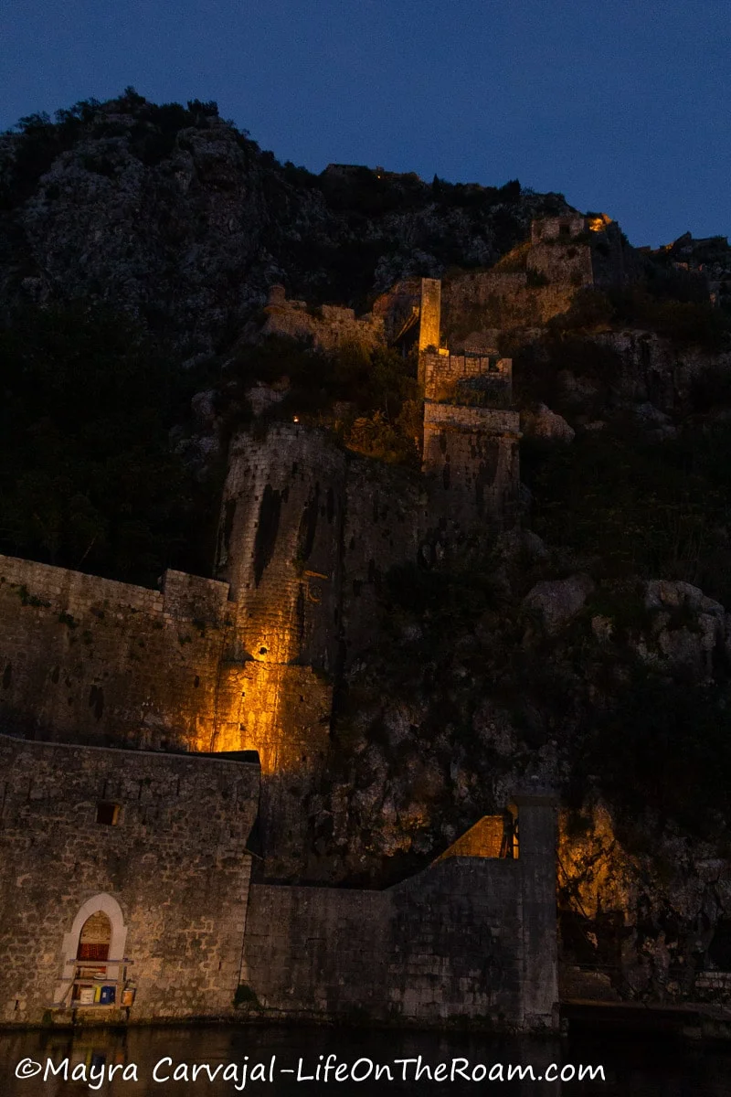 A fortified wall going up the hill with night illumination with an entrance to a fortified town