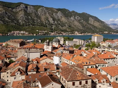 View of the red tiled roofs of houses of an old town with the view of a bay and ridge in the distance