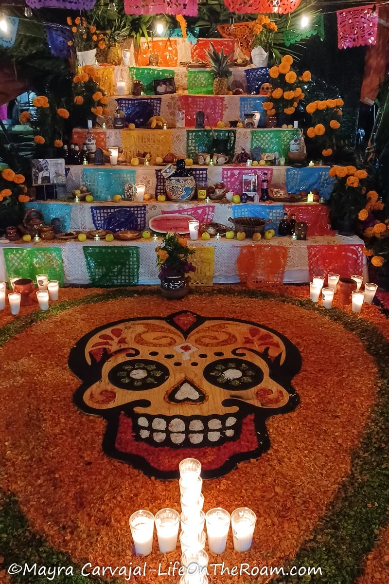 A Day of the Dead altar with a large decorated skull display on the floor with a cross made with candles