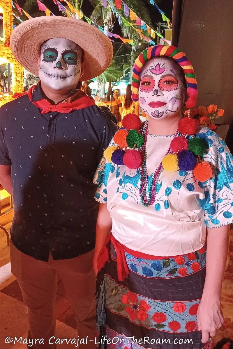 A man and a woman dressed in traditional costumes with their faces painted as skulls