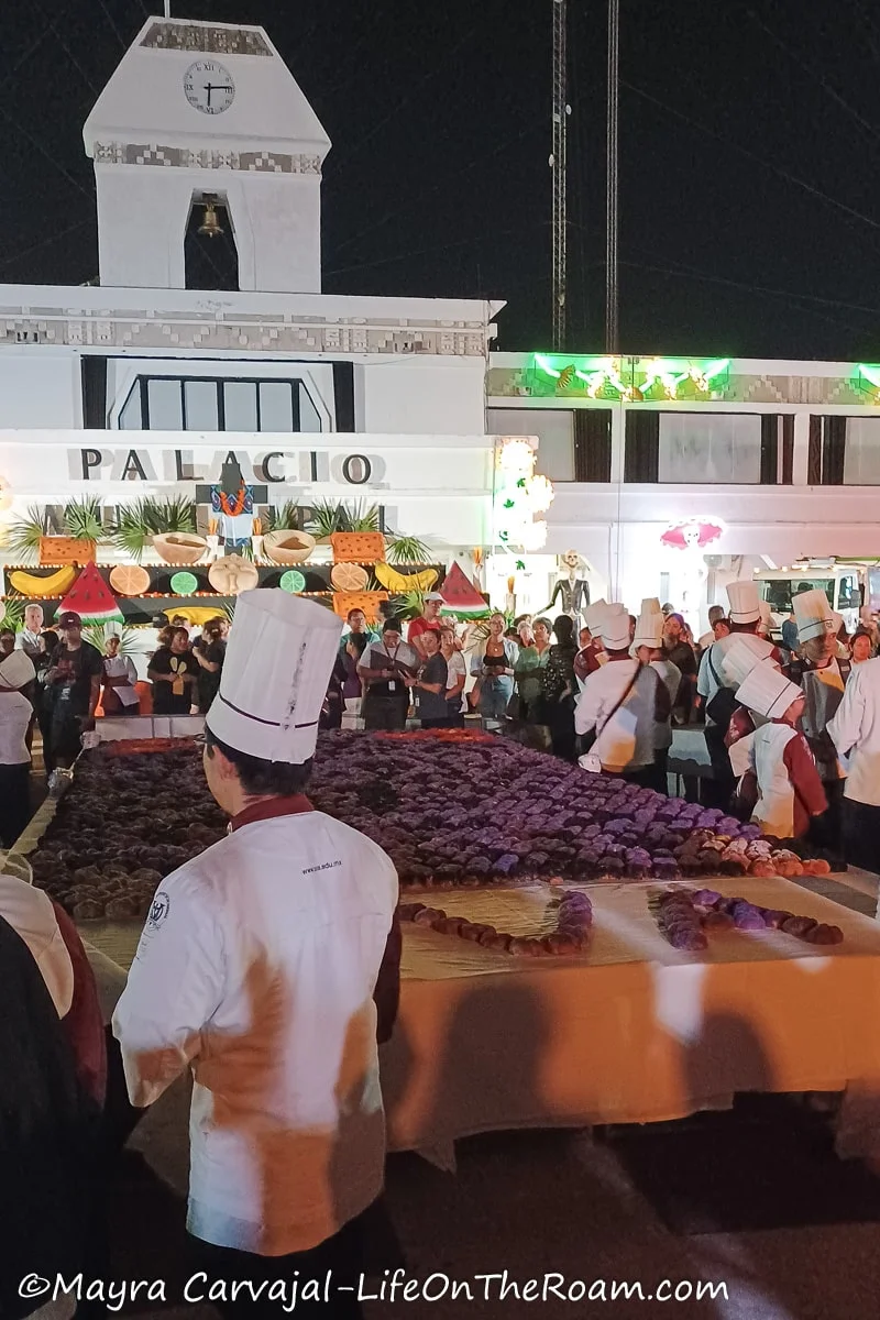 A display of Pan de Muerto in a big table surrounded by people with chef hats in a public square