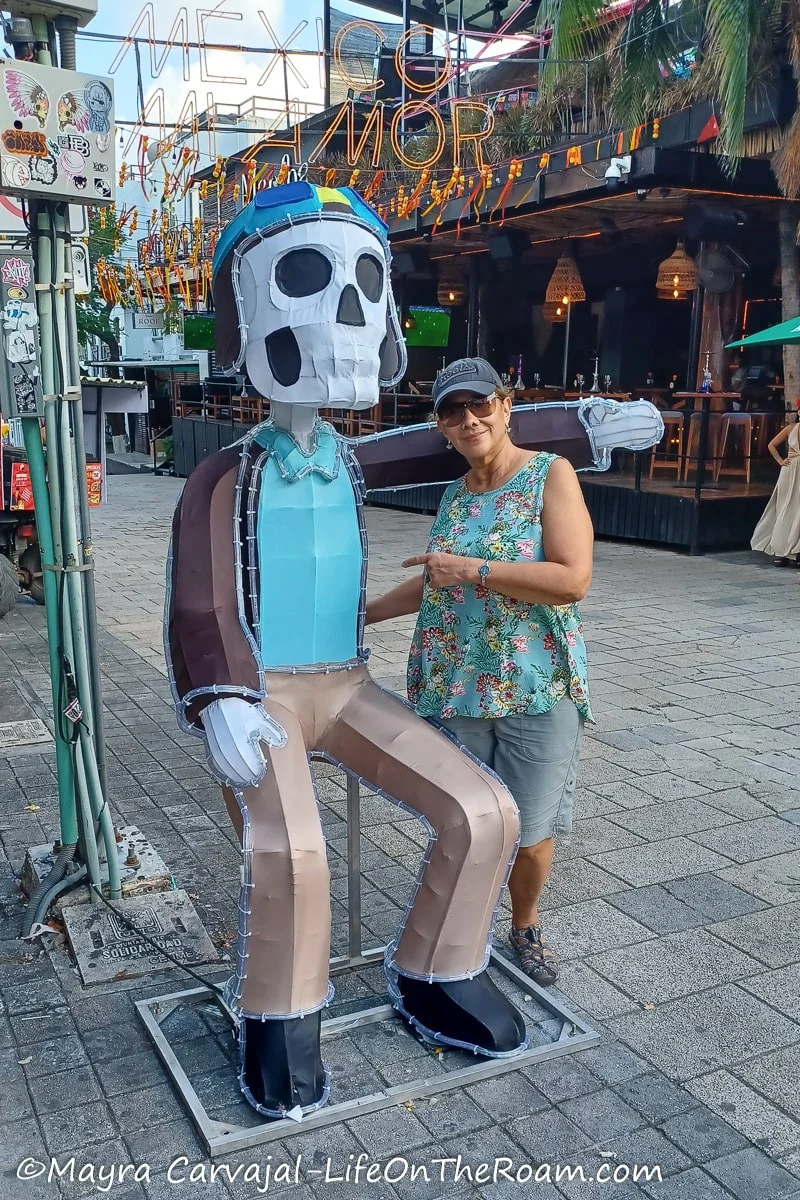 Mayra posing next to a big skeleton-like figure dressed with a hat, jacket, and pants