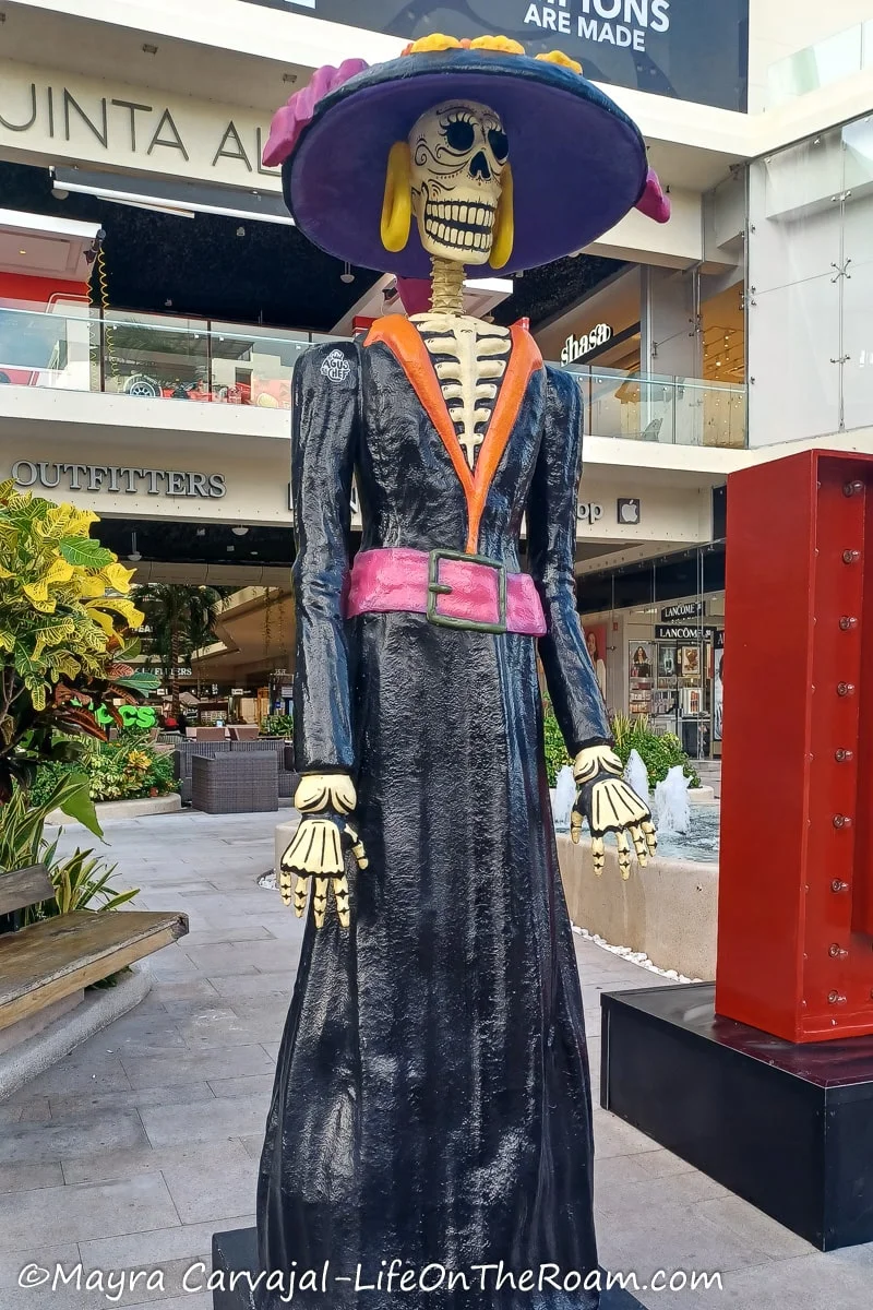 A giant decorated skeleton-like display with a black dress and hat at the entrance of a mall