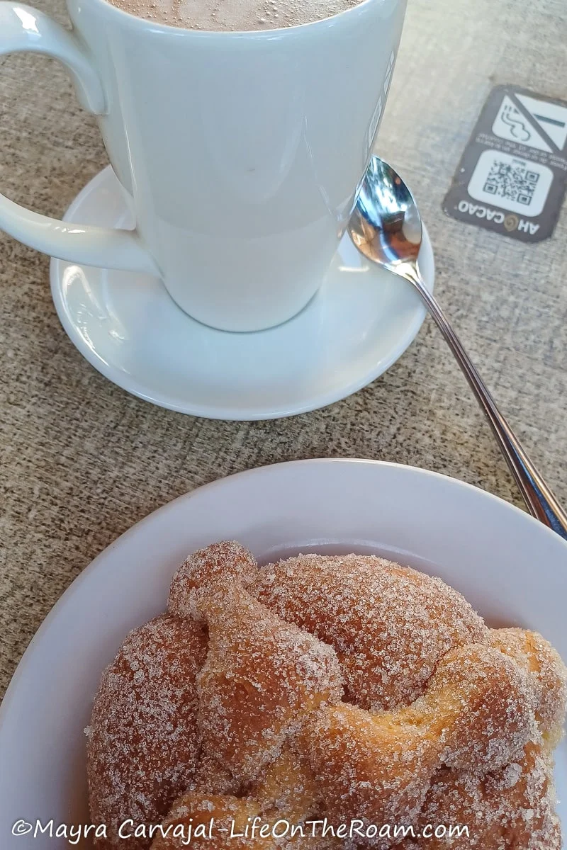 A bun crowned with what looks like crossbones and a white cup and saucer with chocolate