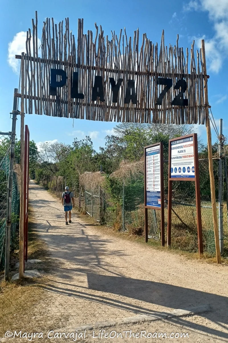 A sign written on palms reading "Playa 72" at the start of a dusty path