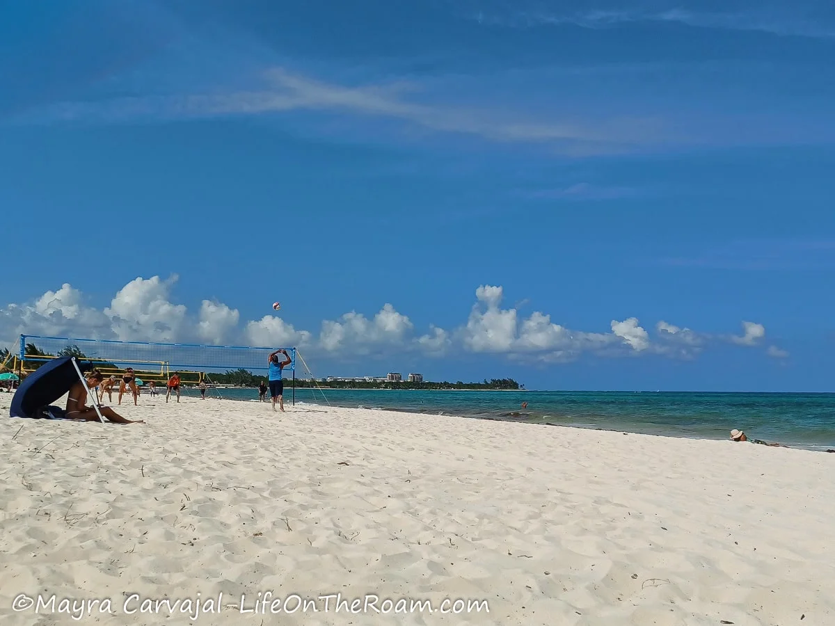 A beach with a wide and long stretch of find sand and a voleyball net