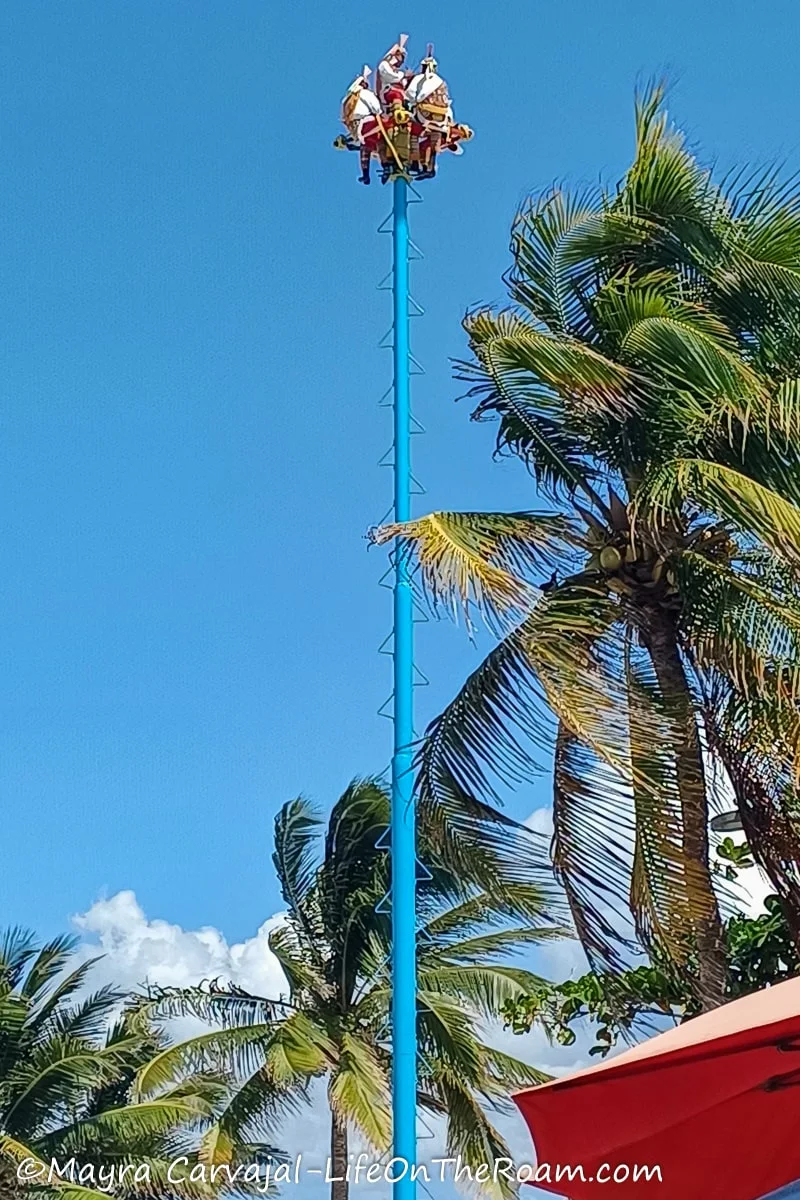 A tall thin blue pole holding a platform with five performers at the top