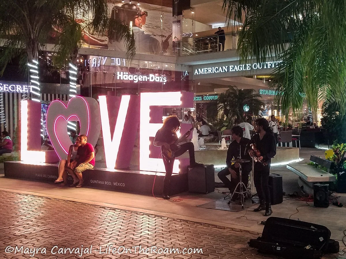 A band playing at night in front of a mall and next to LOVE letter sign