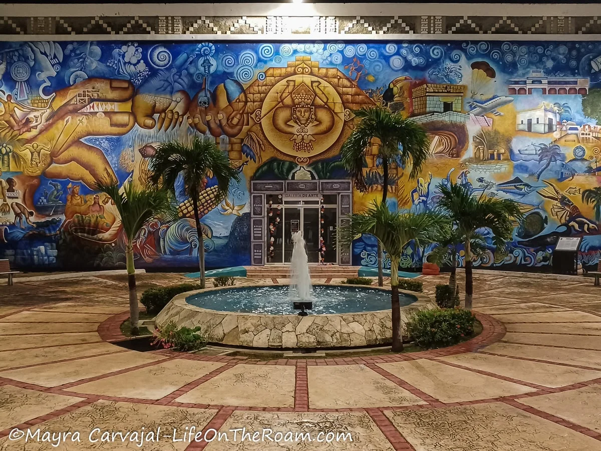 A large mural with a blue background depicting the history of a Mayan town and local fauna