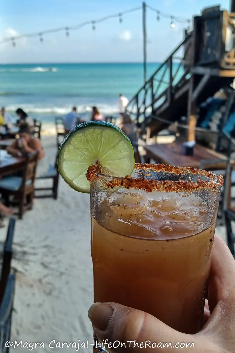 A hand holding a drink with the beach in the background