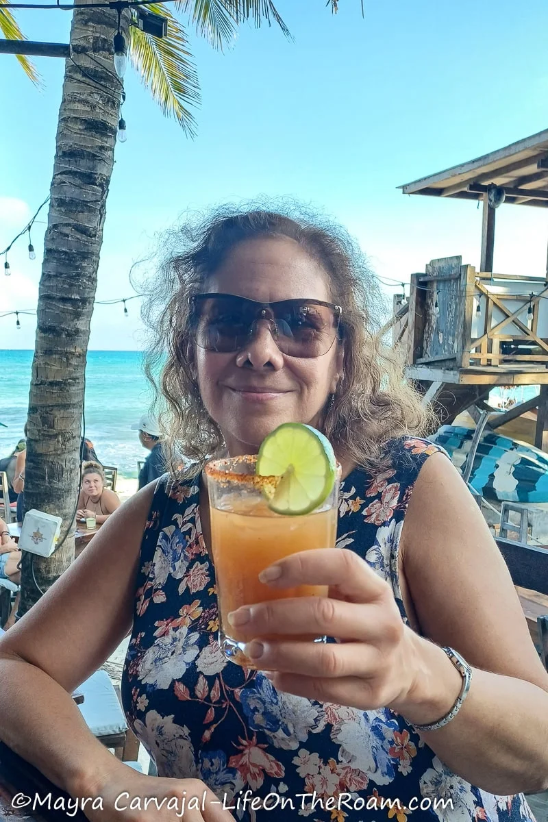 Mayra holding a drink at a beach bar