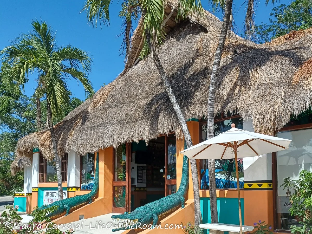 A colorful one-story building with a thatch roof and depictions of crocodiles on the sides