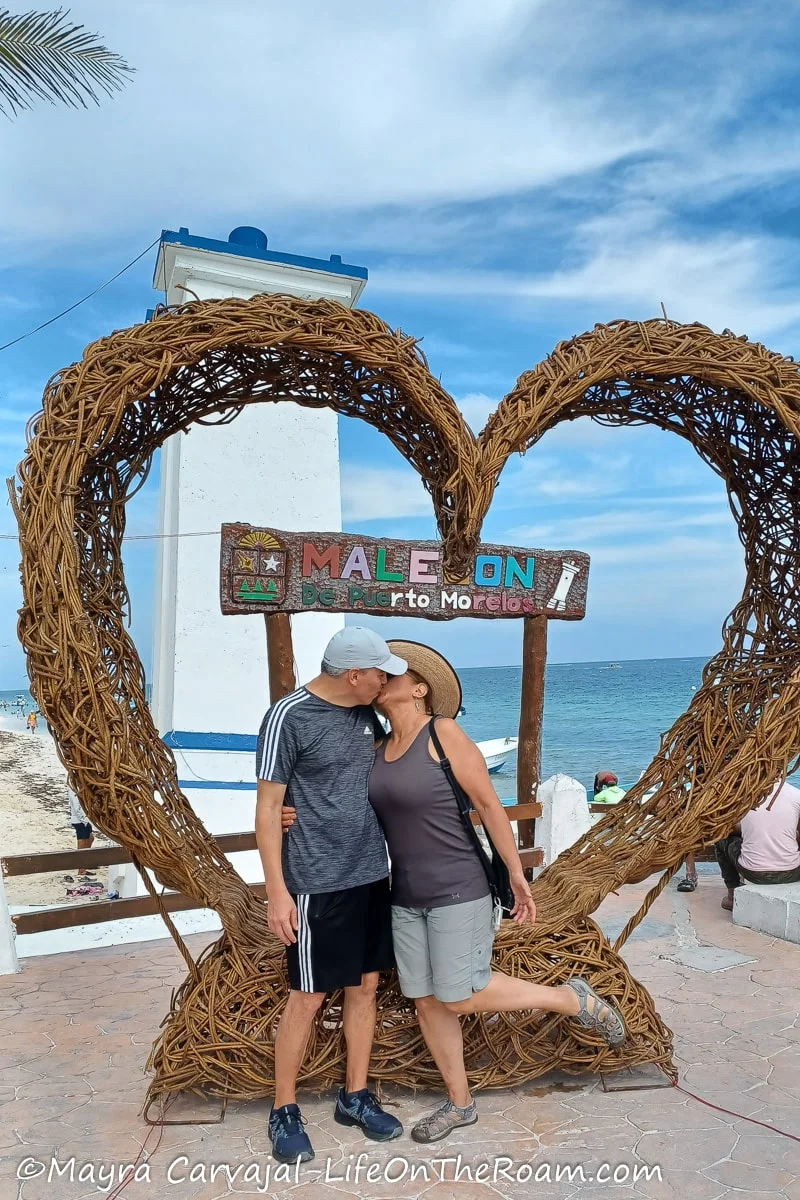 A couple kissing in front of a giant heart placed on a beach boardwalk