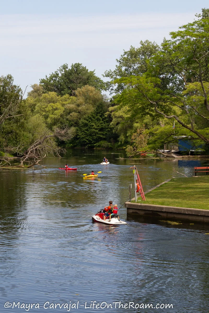 People on kayaks and jet skis on a canal flanked with trees