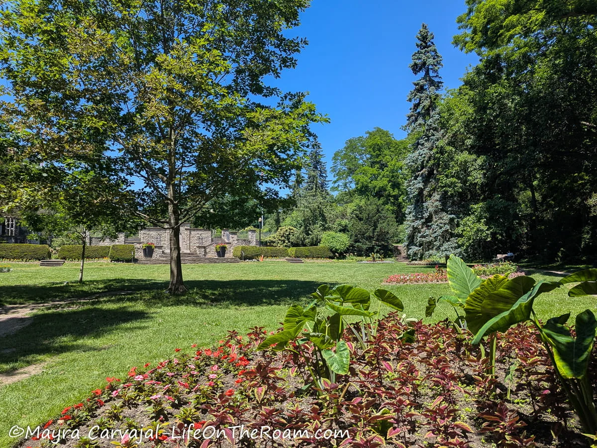 An urban park with a large grass patch and manicured gardens