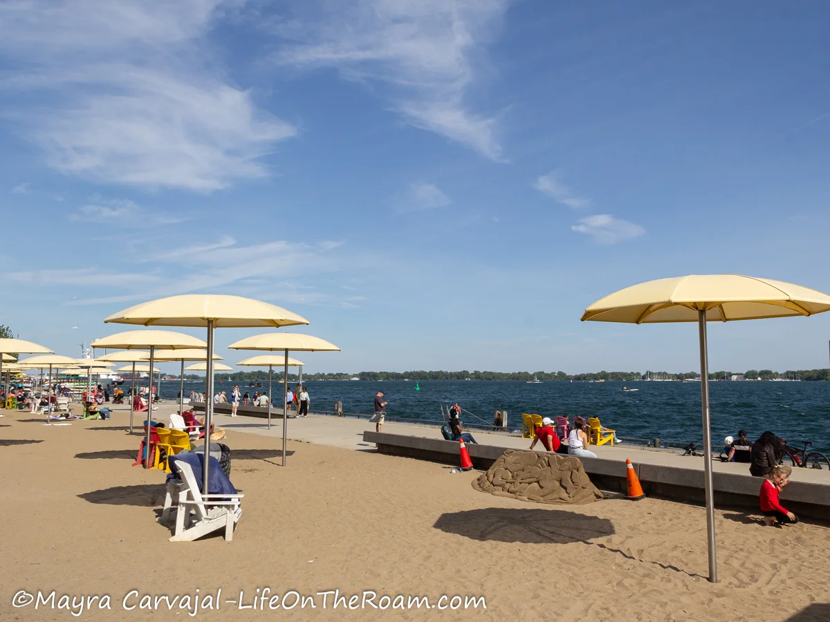 A sand strip on a lakefront promenade with yellow umbrellas and lounge chairs