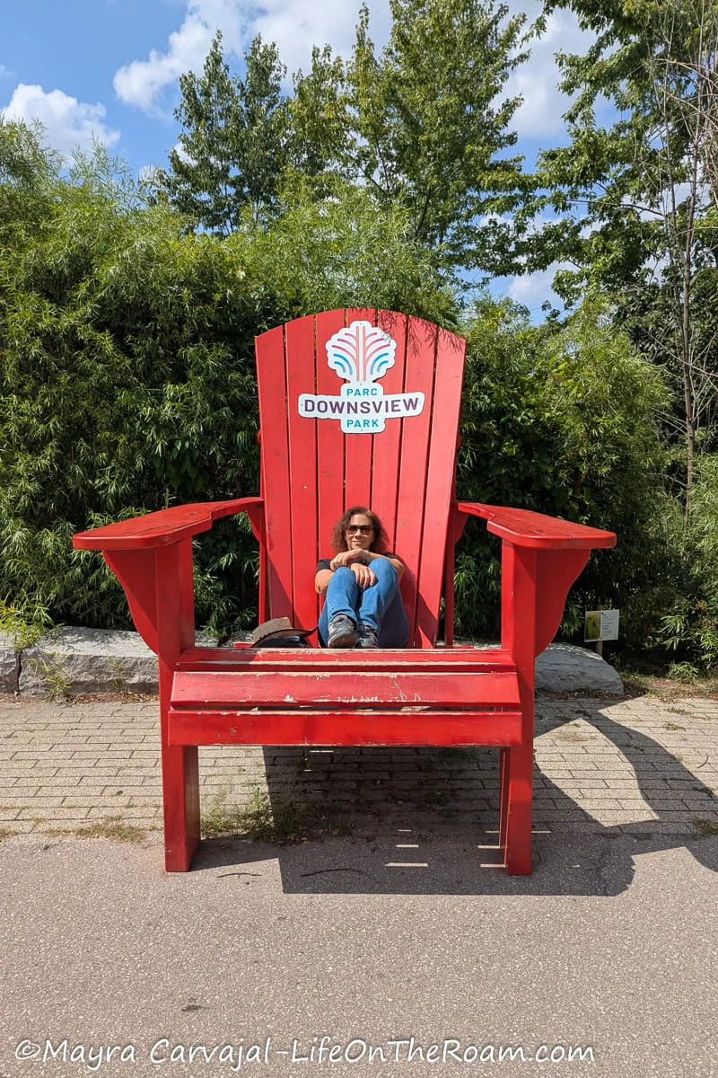 Mayra sitting on a giant red Muskoka chair in a park